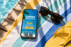 Mobile phone displaying a summer sweepstakes promotion on a beach towel with sunglasses and flip-flops